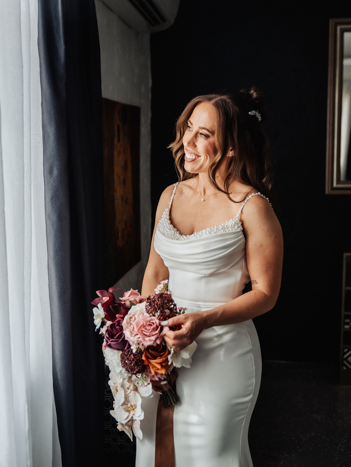 the lane vineyard wedding - caitlyn & craig 90 Woman in elegant white gown holding vibrant bouquet gazes out window serenely.