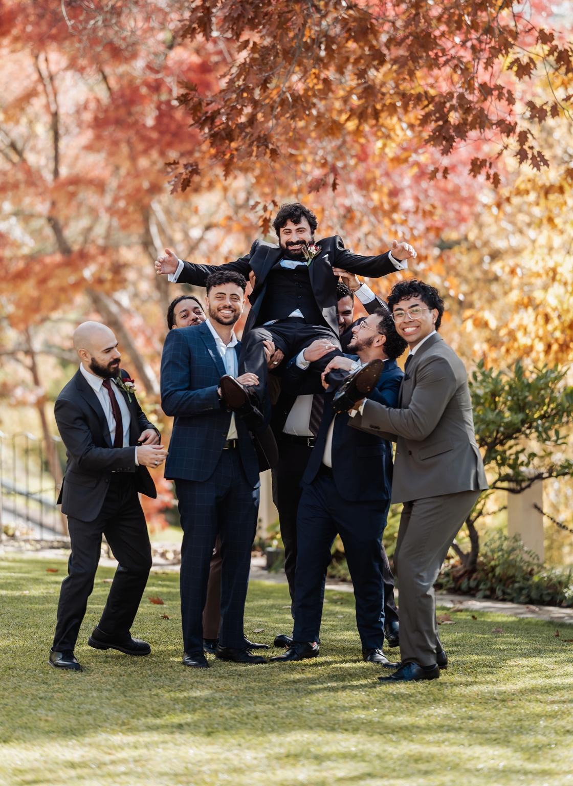 beautiful manor basket range wedding - sophie & theodore 85 Men celebrate outdoors, lifting friend in suits during autumn event.