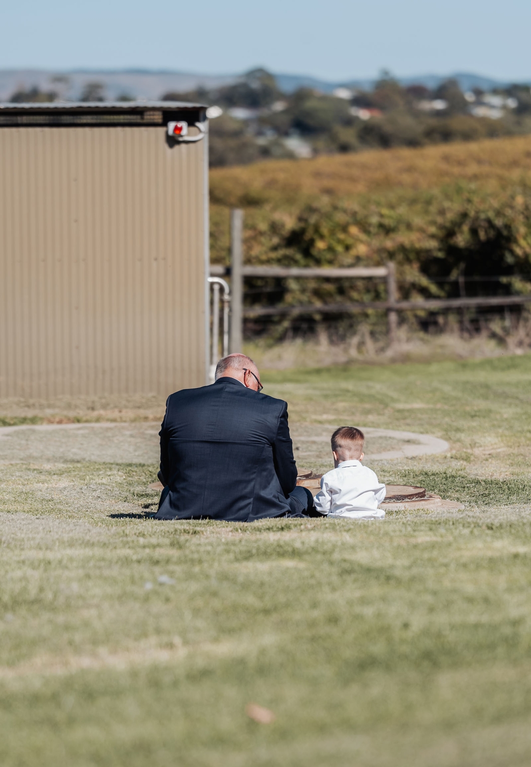 lloyd brothers wedding - dajana & tom 40 Older man and young boy bonding in a tranquil vineyard setting under a clear sky.