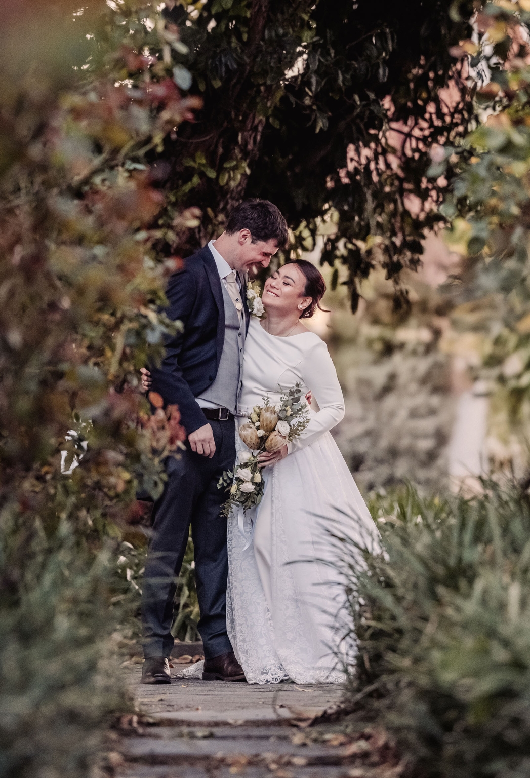 adelaide's st peter's cathedral wedding - irish & nick 49 Bride and groom share a joyful wedding portrait on a lush garden path.