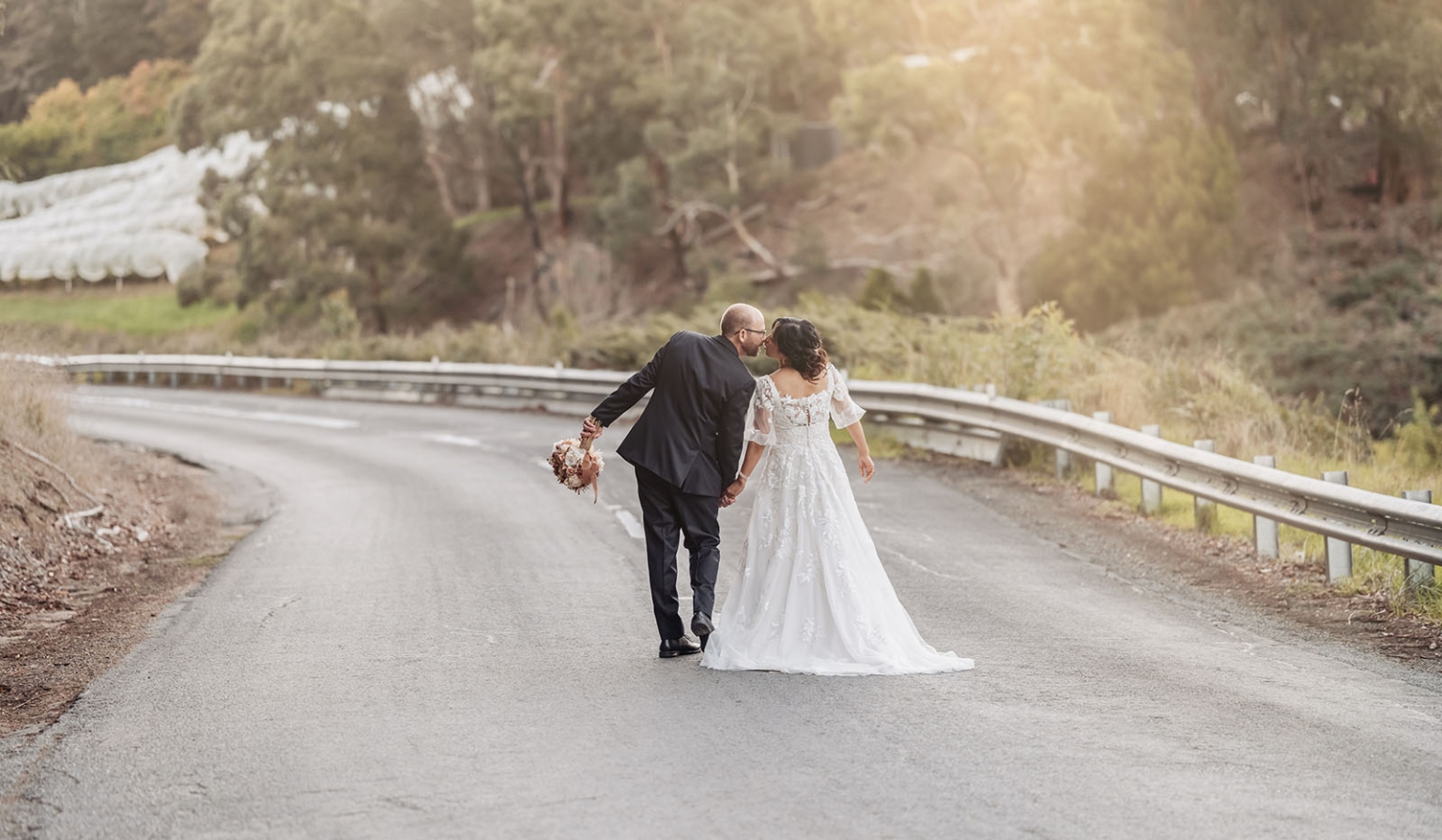 adelaide hills wedding at the manor - jo & dan 50 Newlywed couple kissing on a country road during golden hour wedding portraits.