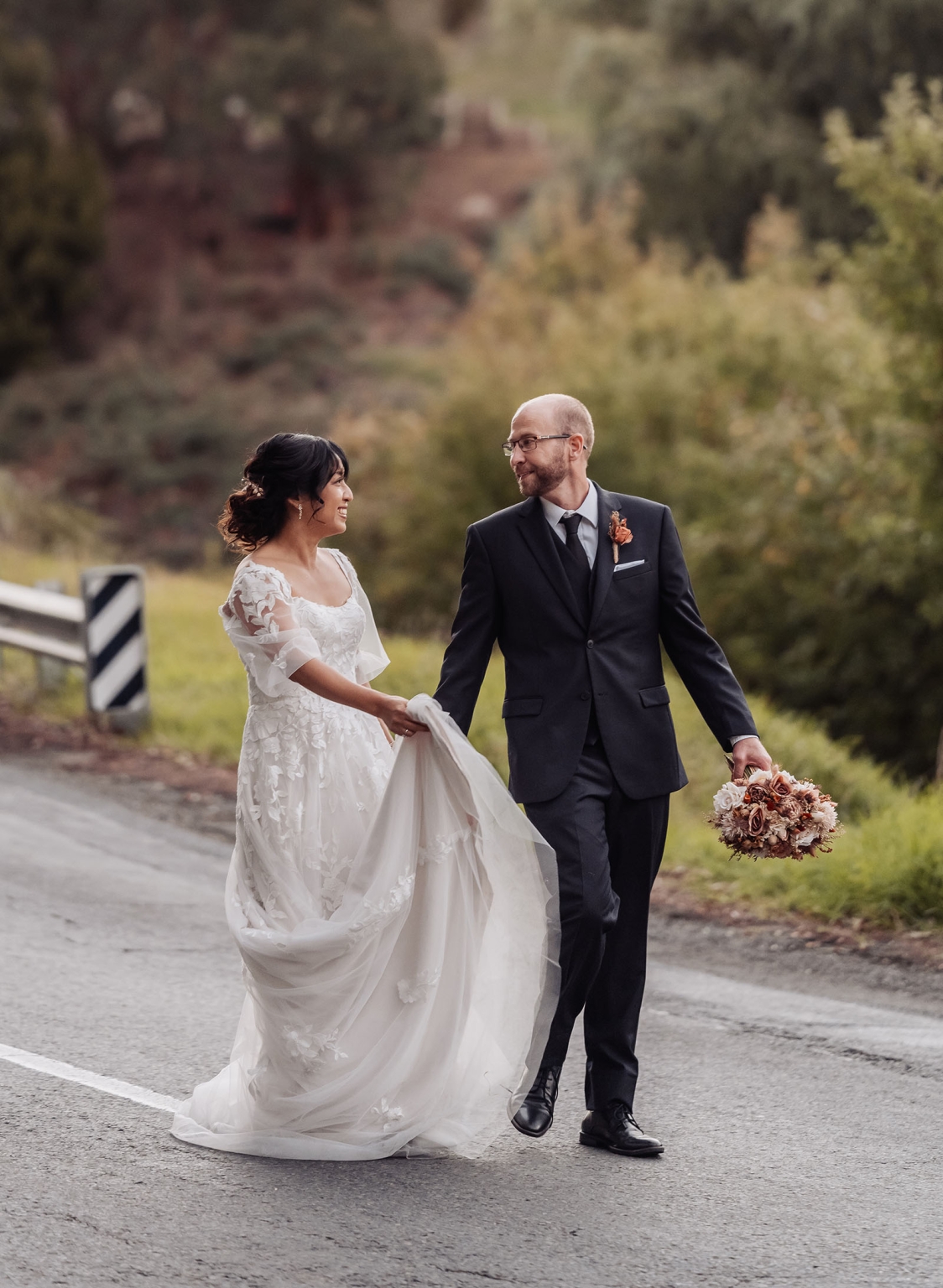 adelaide hills wedding at the manor - jo & dan 55 Newlywed couple walking on scenic road after romantic outdoor wedding.