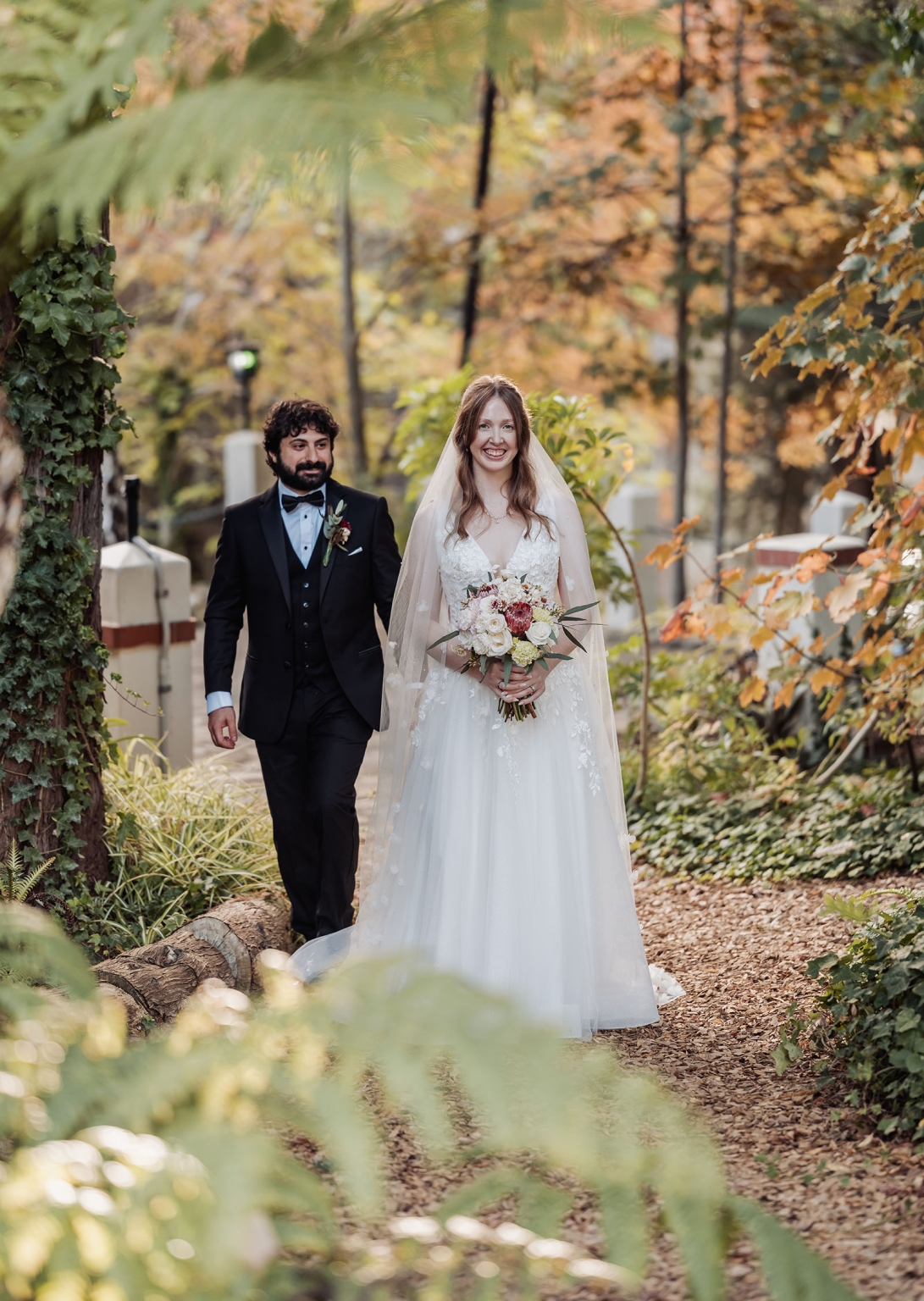 beautiful manor basket range wedding - sophie & theodore 118 Bride and groom walking on a scenic autumn forest path in wedding attire.