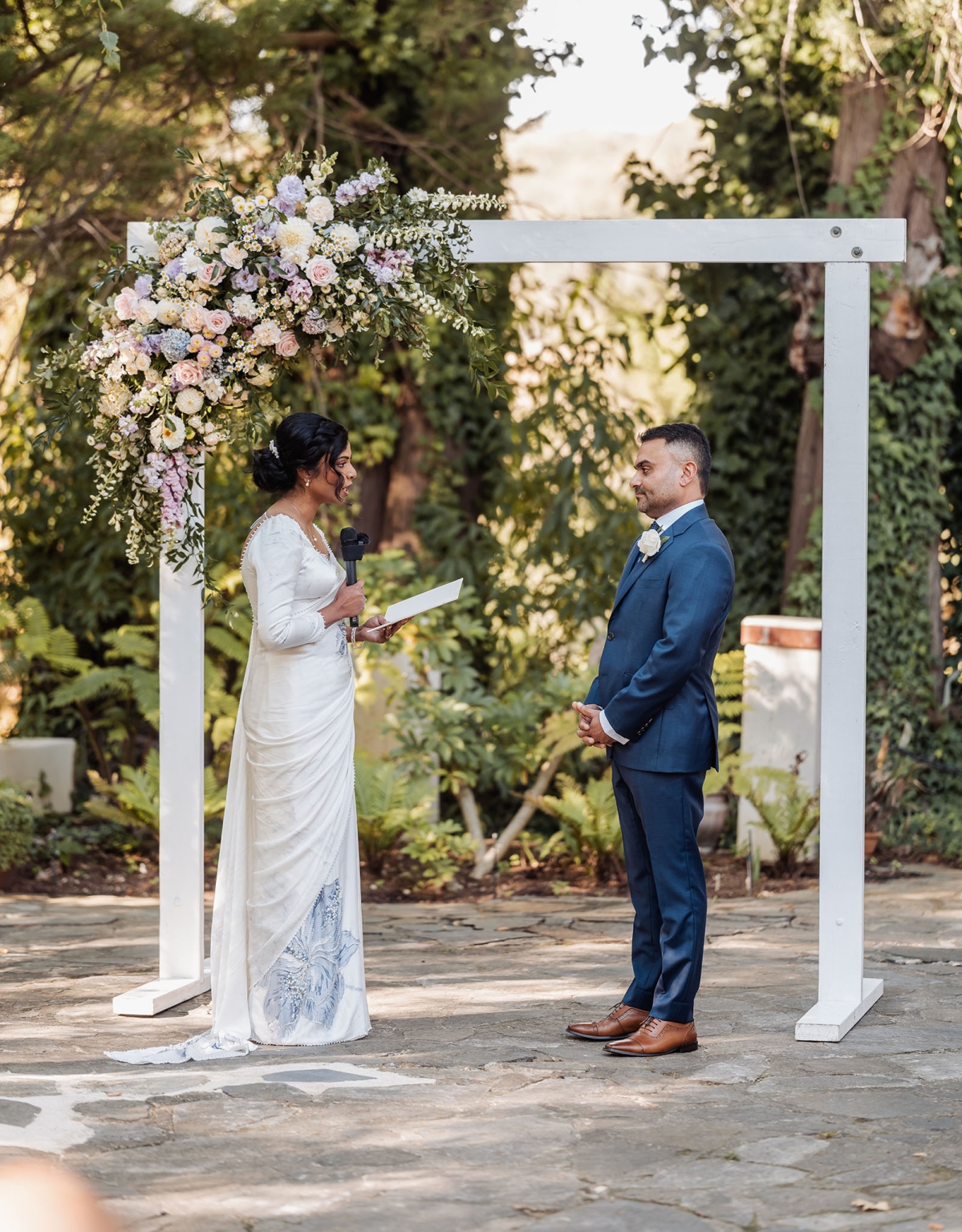 manor wedding in basket range - methmini & aravinda 141 Elegant outdoor wedding ceremony under a floral arch with bride and groom exchanging vows.