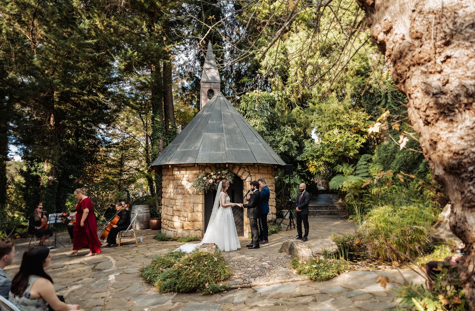 beautiful manor basket range wedding - sophie & theodore 106 Outdoor wedding by rustic chapel in forest, bride, groom, musicians, guests, nature backdrop.