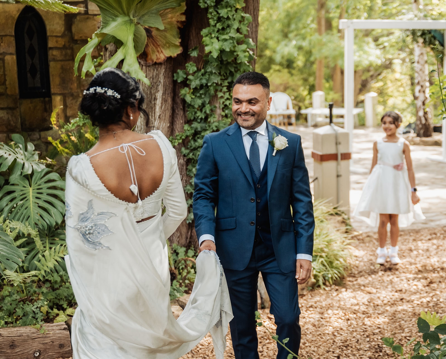manor wedding in basket range - methmini & aravinda 127 Elegant garden wedding scene with bride, groom, lush greenery, and flower girl in white dress.