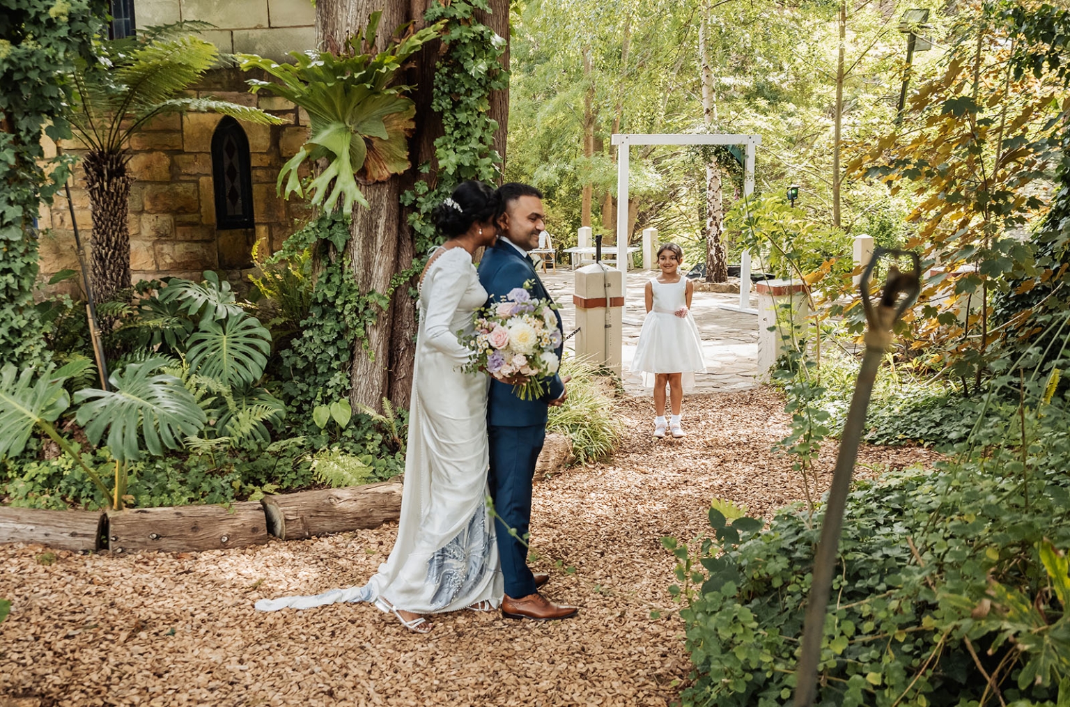 manor wedding in basket range - methmini & aravinda 124 Outdoor garden wedding with newlyweds, a flower girl, and lush greenery backdrop.