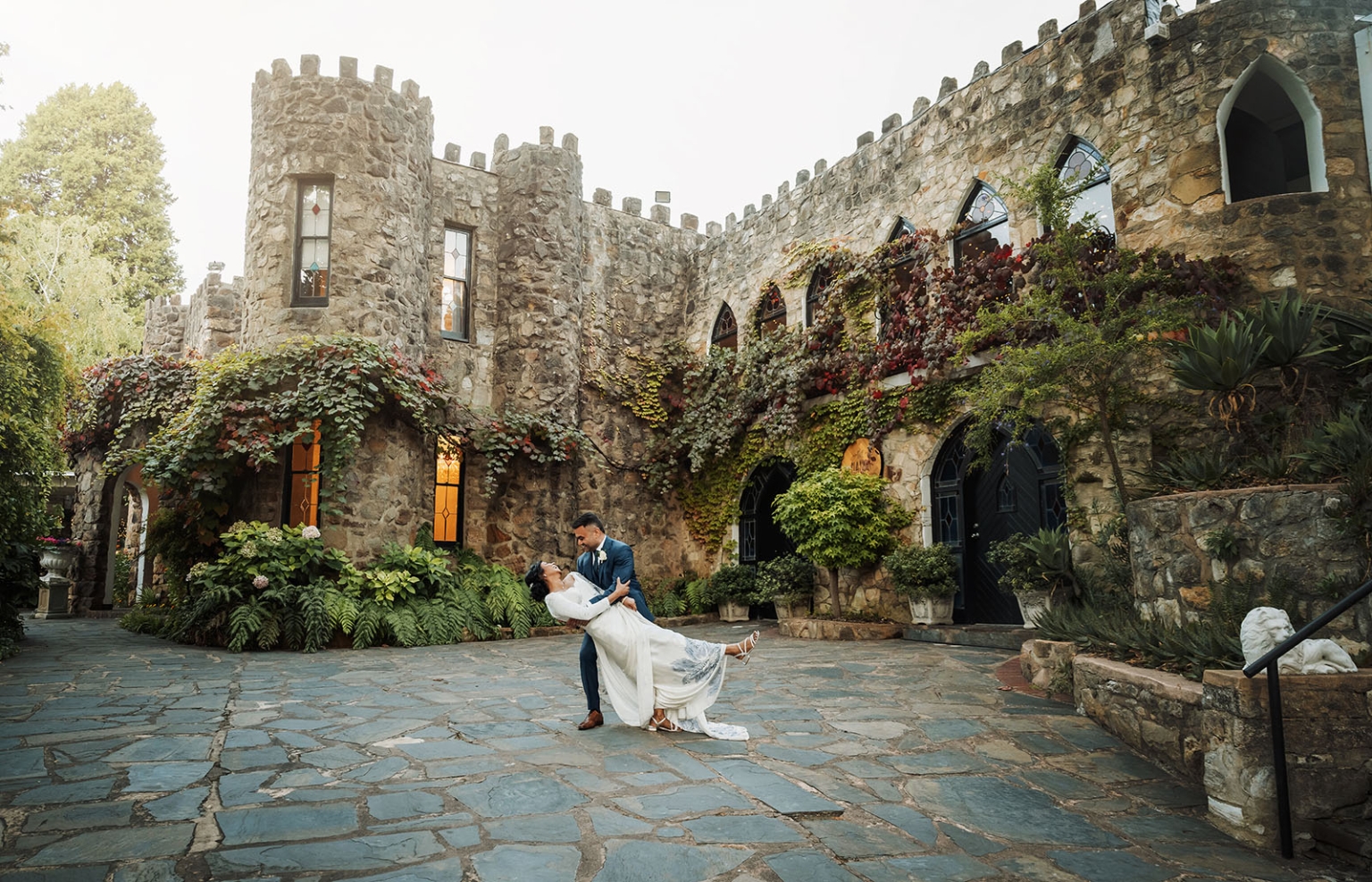 manor wedding in basket range - methmini & aravinda 159 Couple dancing romantically by historic ivy-covered castle with cobblestone path.