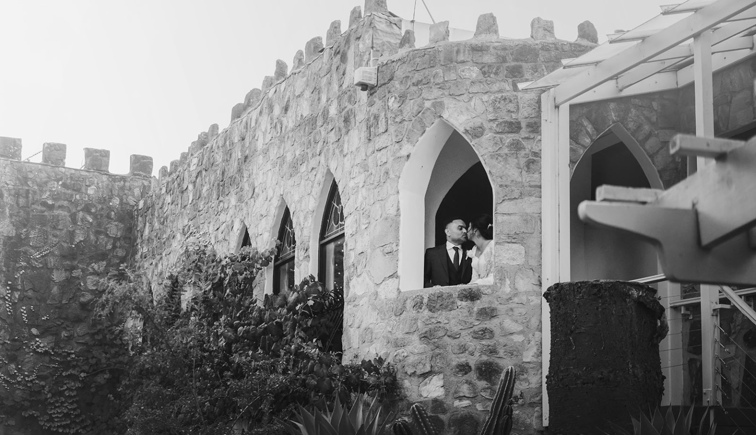 manor wedding in basket range - methmini & aravinda 156 Romantic couple kissing in stone castle archway surrounded by gothic architecture and greenery.