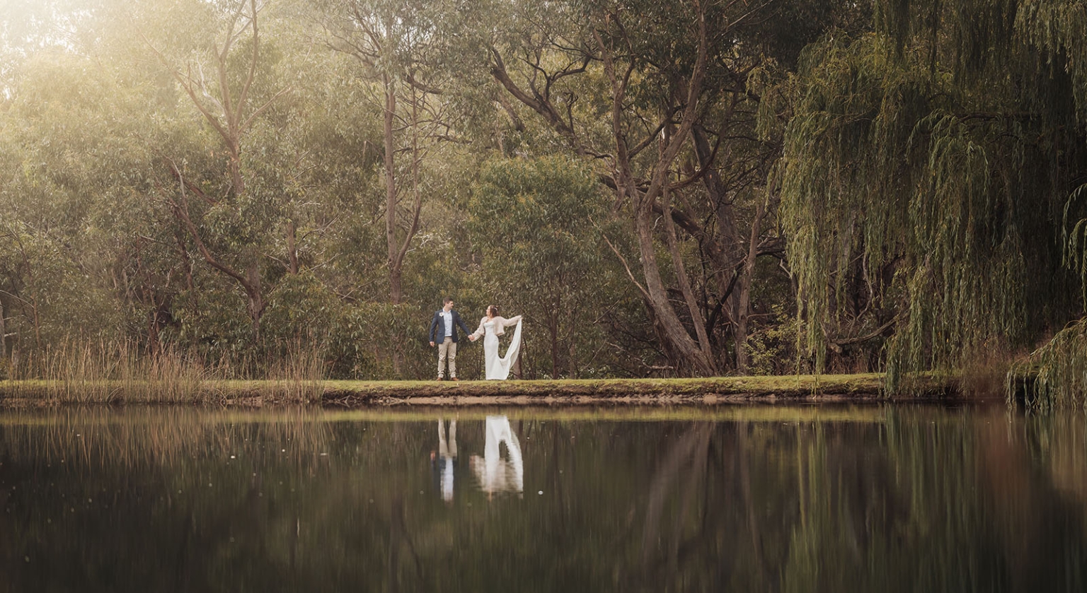 the lane vineyard wedding - caitlyn & craig 113 Couple stands by tranquil lake, surrounded by trees and mirrored reflections, evoking serenity.