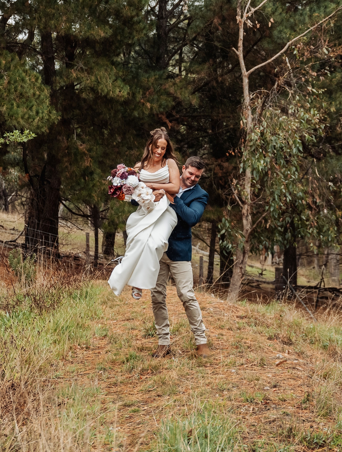 the lane vineyard wedding - caitlyn & craig 111 Joyful couple in forest, woman in wedding dress lifted by man.