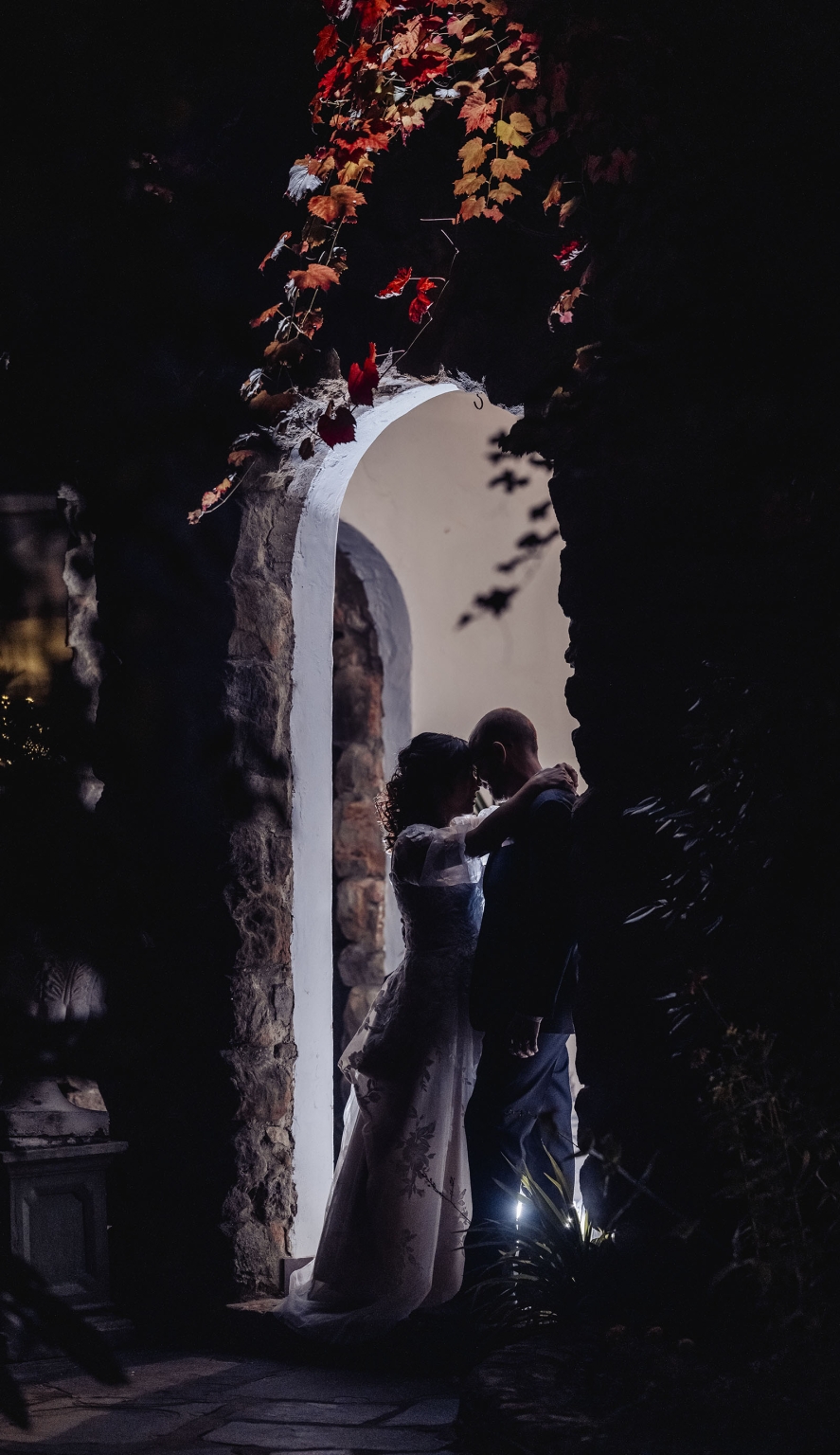 adelaide hills wedding at the manor - jo & dan 77 Romantic wedding couple embracing beneath autumn vines and a rustic stone arch.