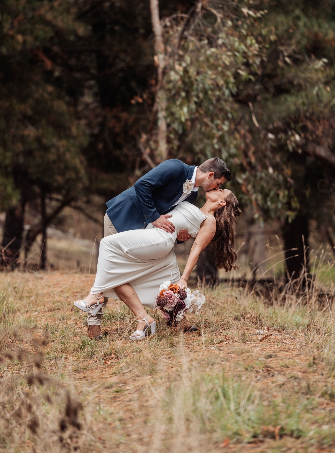 the lane vineyard wedding - caitlyn & craig 110 Bride and groom share romantic kiss in autumn forest with vibrant flowers.