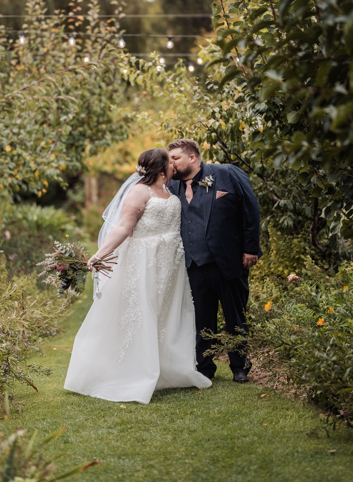 comida wedding - georgia & james 29 Bride and groom kiss in lush garden, elegant wedding scene.