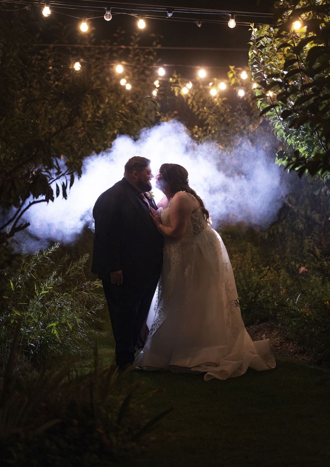 comida wedding - georgia & james 56 Bride and groom in romantic, misty garden evening wedding with string lights and greenery.