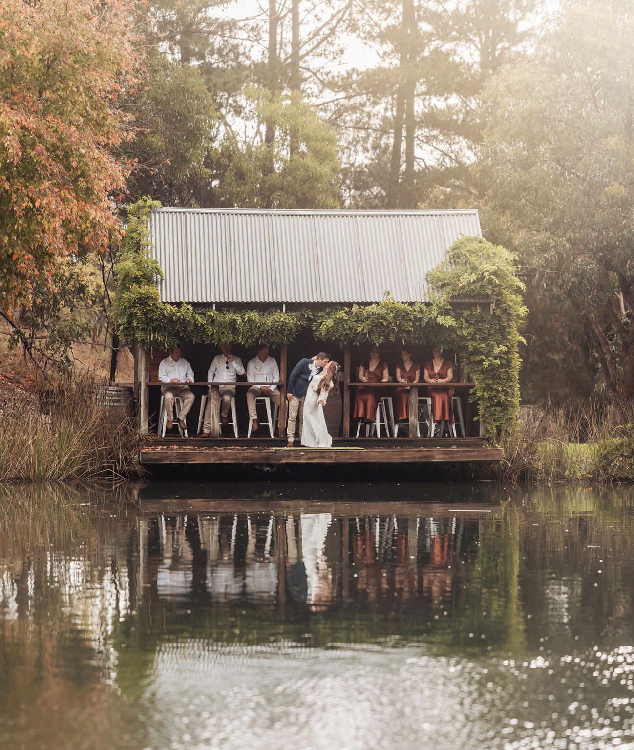 the lane vineyard wedding - caitlyn & craig 112 Bride and groom embracing at lakeside boathouse wedding with friends and autumn trees.