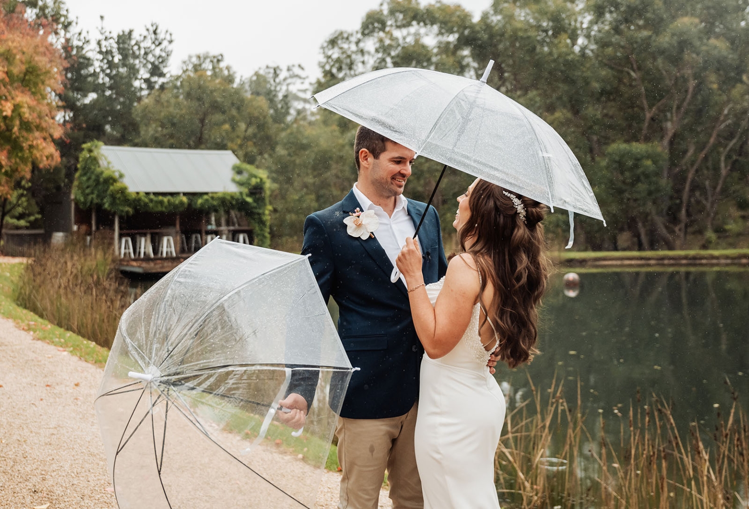 the lane vineyard wedding - caitlyn & craig 101 Elegant couple embraces by a tranquil lake with clear umbrellas, exuding romance and joy.