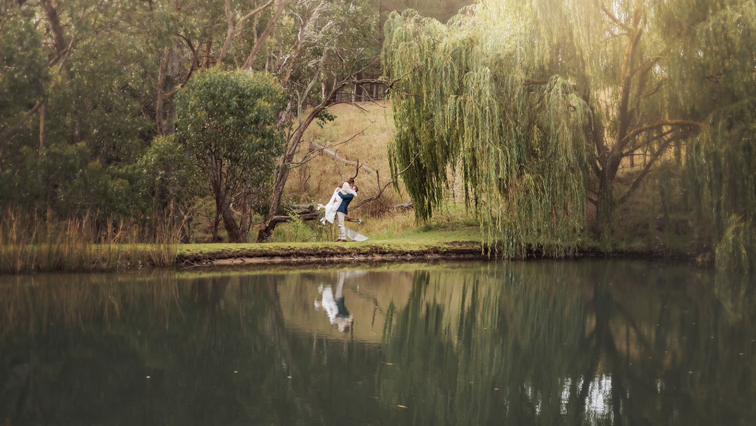 the lane vineyard wedding - caitlyn & craig 103 Bride and groom embrace by pond under willow tree, reflecting love and natures beauty.