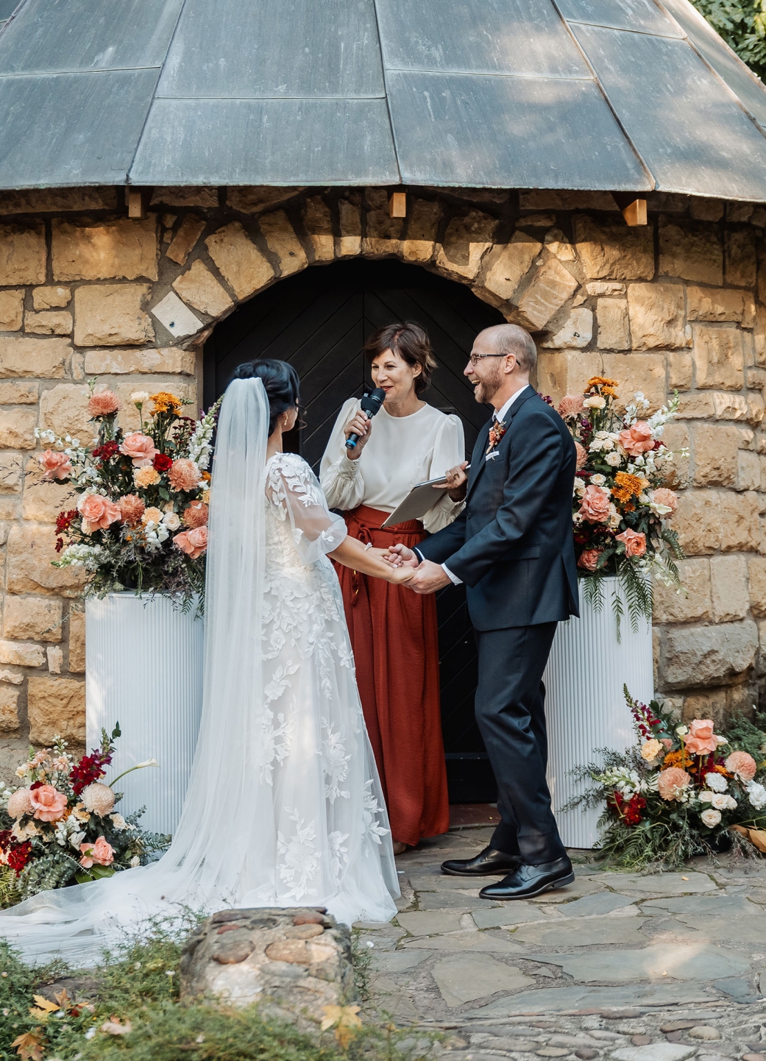 adelaide hills wedding at the manor - jo & dan 26 Rustic stone arch wedding ceremony with bride, groom, officiant, and romantic florals.