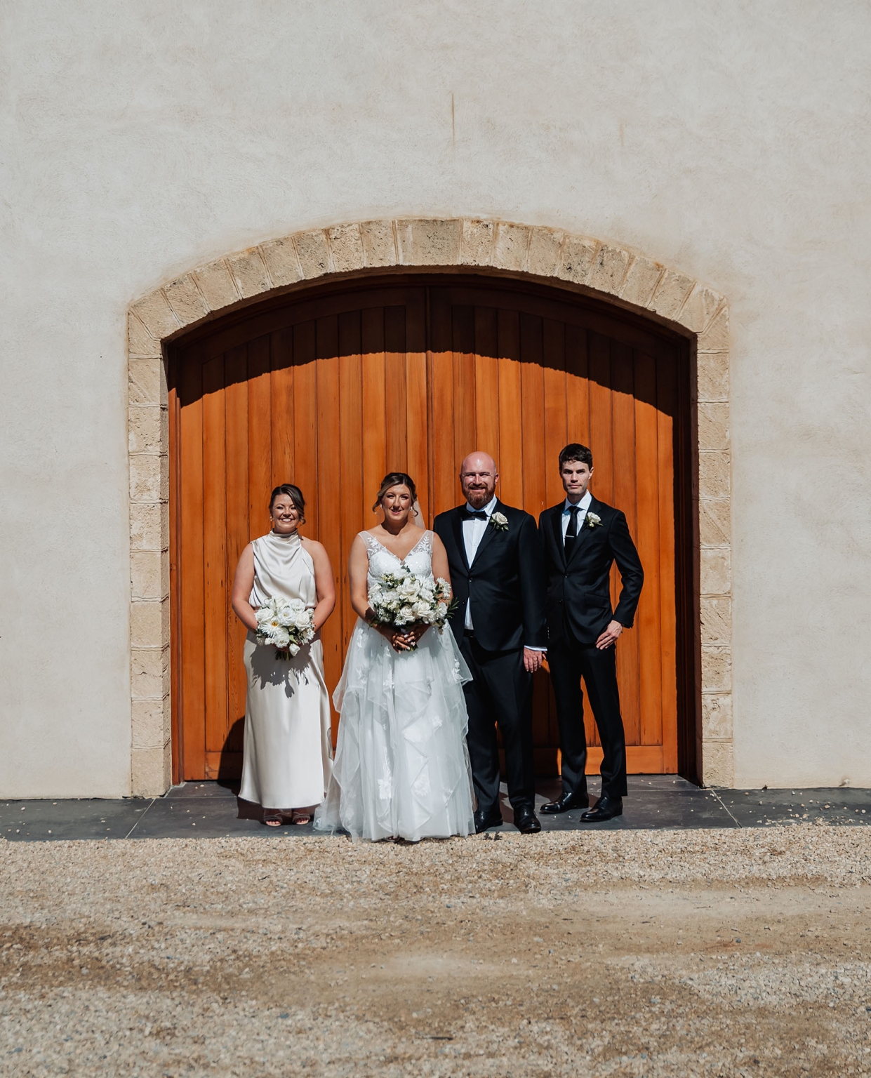 lloyd brothers wedding - dajana & tom 24 Elegant outdoor wedding with bride, groom, and bridal party in rustic stone archway setting.