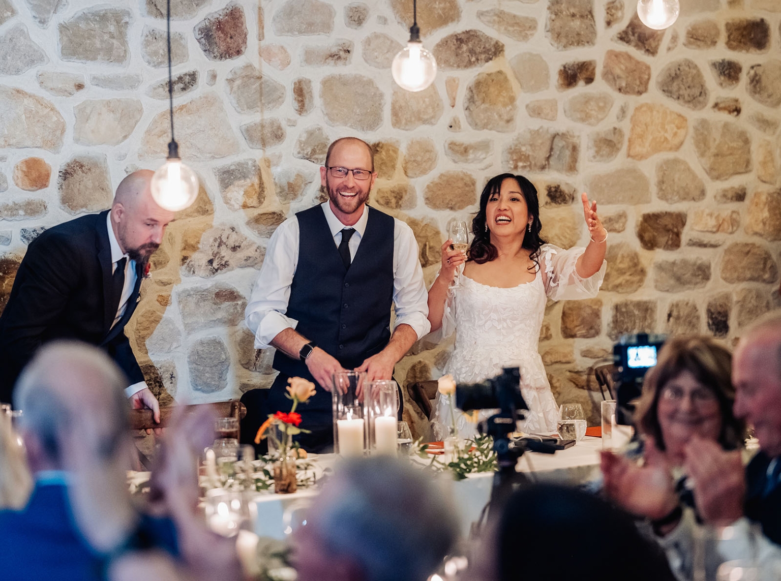 adelaide hills wedding at the manor - jo & dan 65 Bride gives toast at rustic wedding reception with stone wall and warm lights.