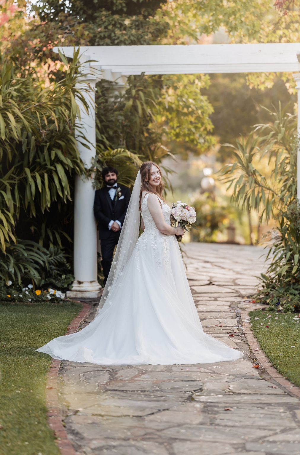 beautiful manor basket range wedding - sophie & theodore 112 Bride and groom in elegant garden wedding scene with lush greenery.