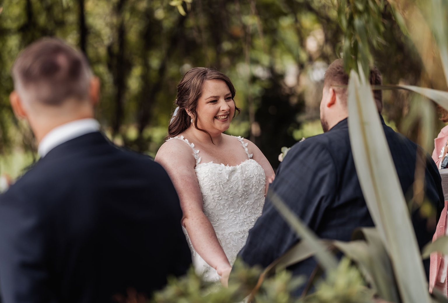 comida wedding - georgia & james 15 Bride in floral gown at serene outdoor wedding ceremony, surrounded by lush greenery.