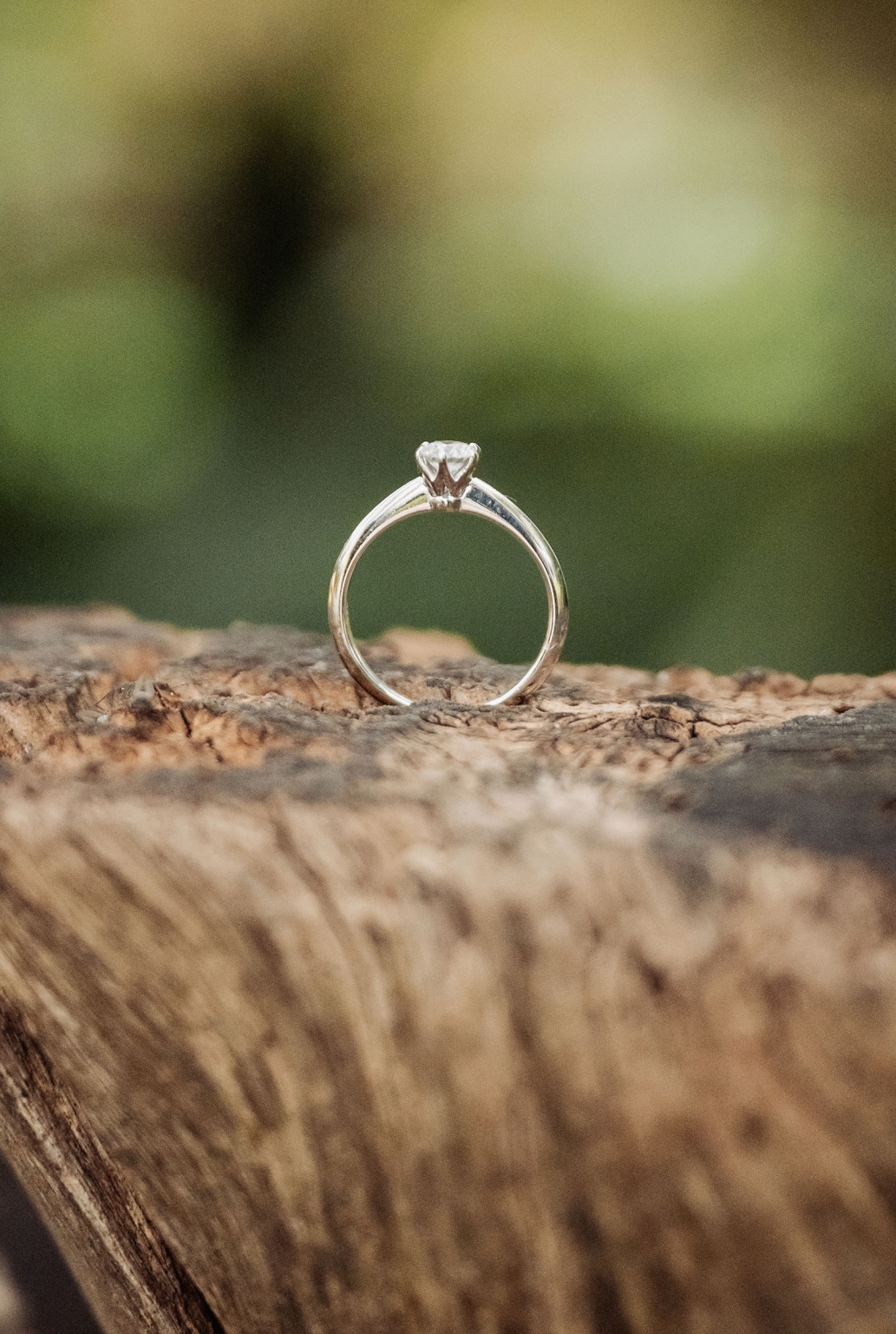 comida wedding - georgia & james 40 Engagement ring with diamond on rustic wood surface, blurred outdoor background.