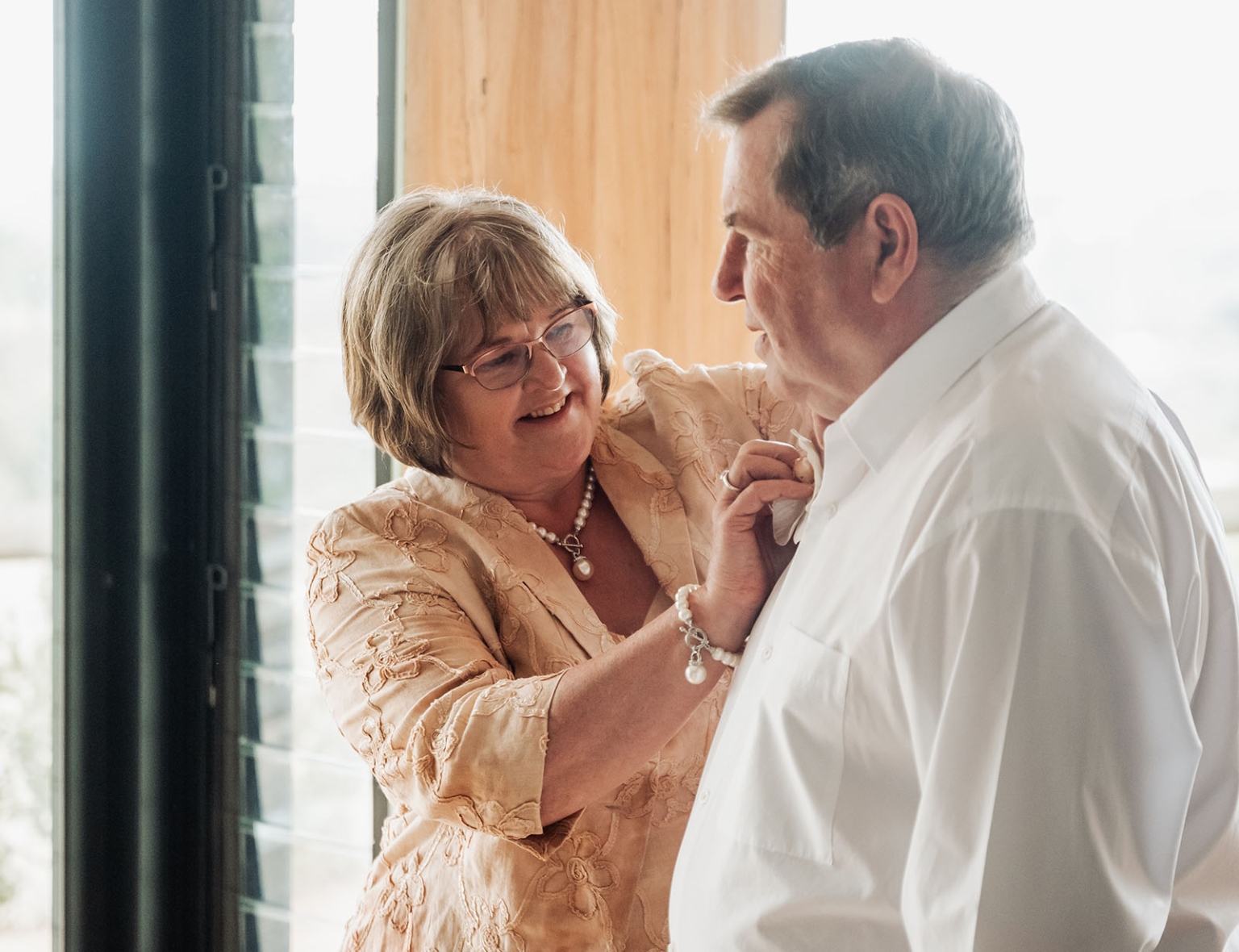 the lane vineyard wedding - caitlyn & craig 73 Older couple sharing a loving, intimate moment by a sunlit window.