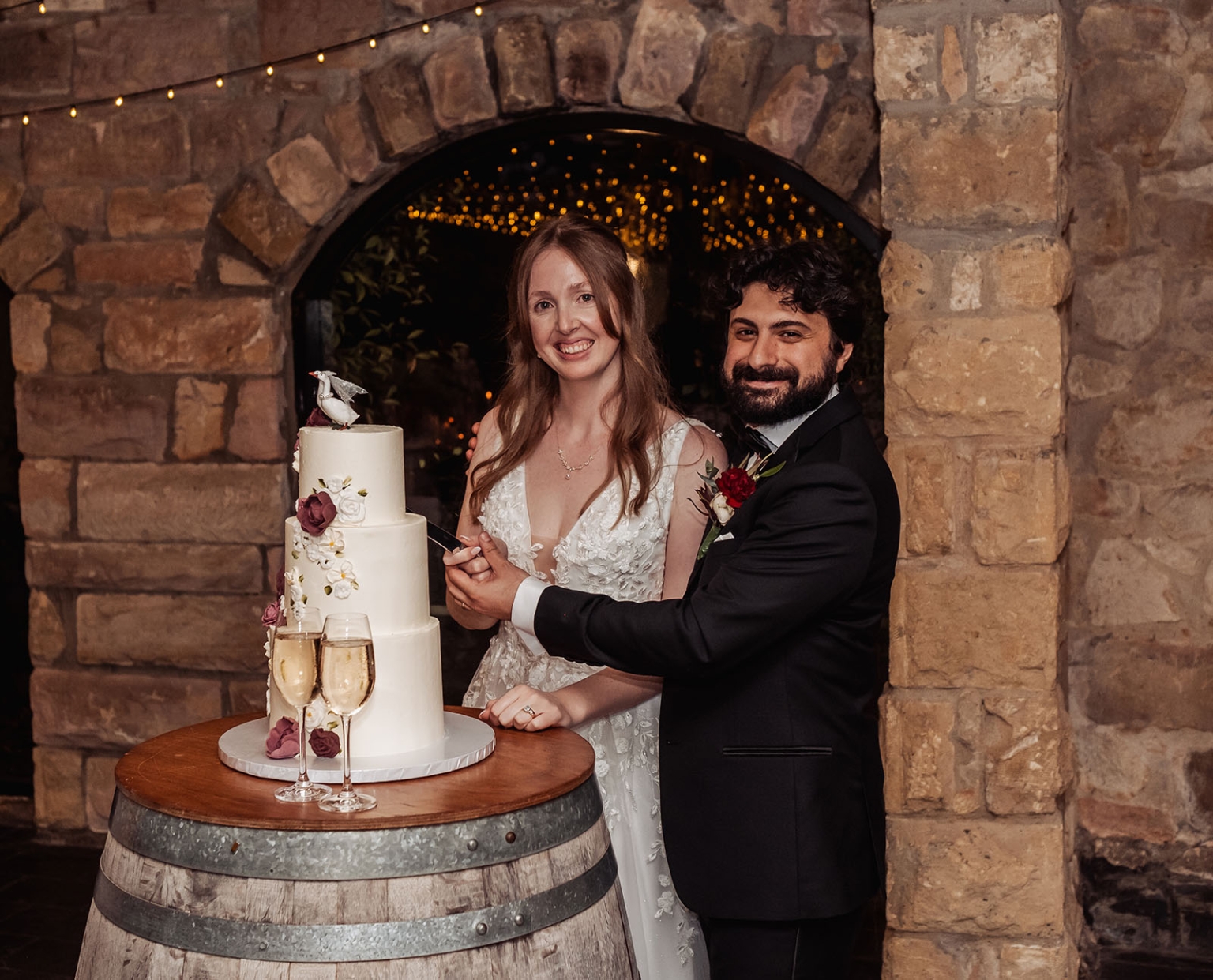 beautiful manor basket range wedding - sophie & theodore 143 Bride and groom cutting wedding cake at rustic reception under stone arch.