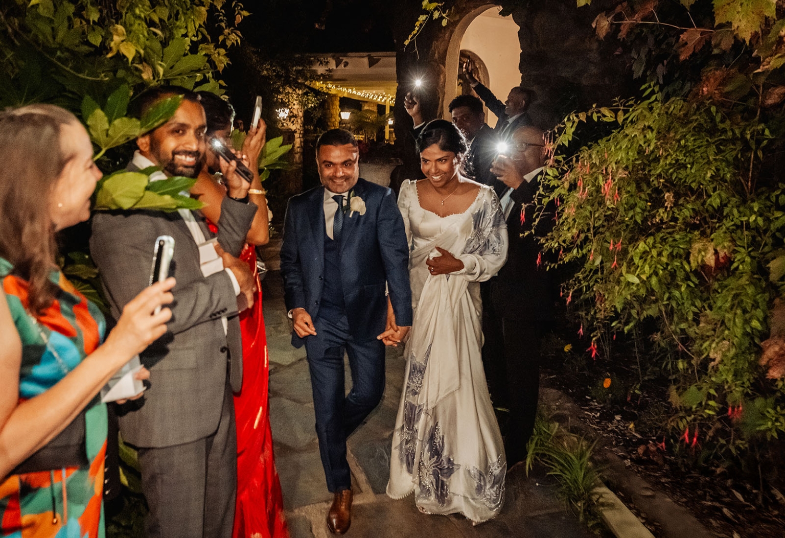 manor wedding in basket range - methmini & aravinda 176 Joyful wedding couple in elegant attire, surrounded by guests in a lush garden setting.