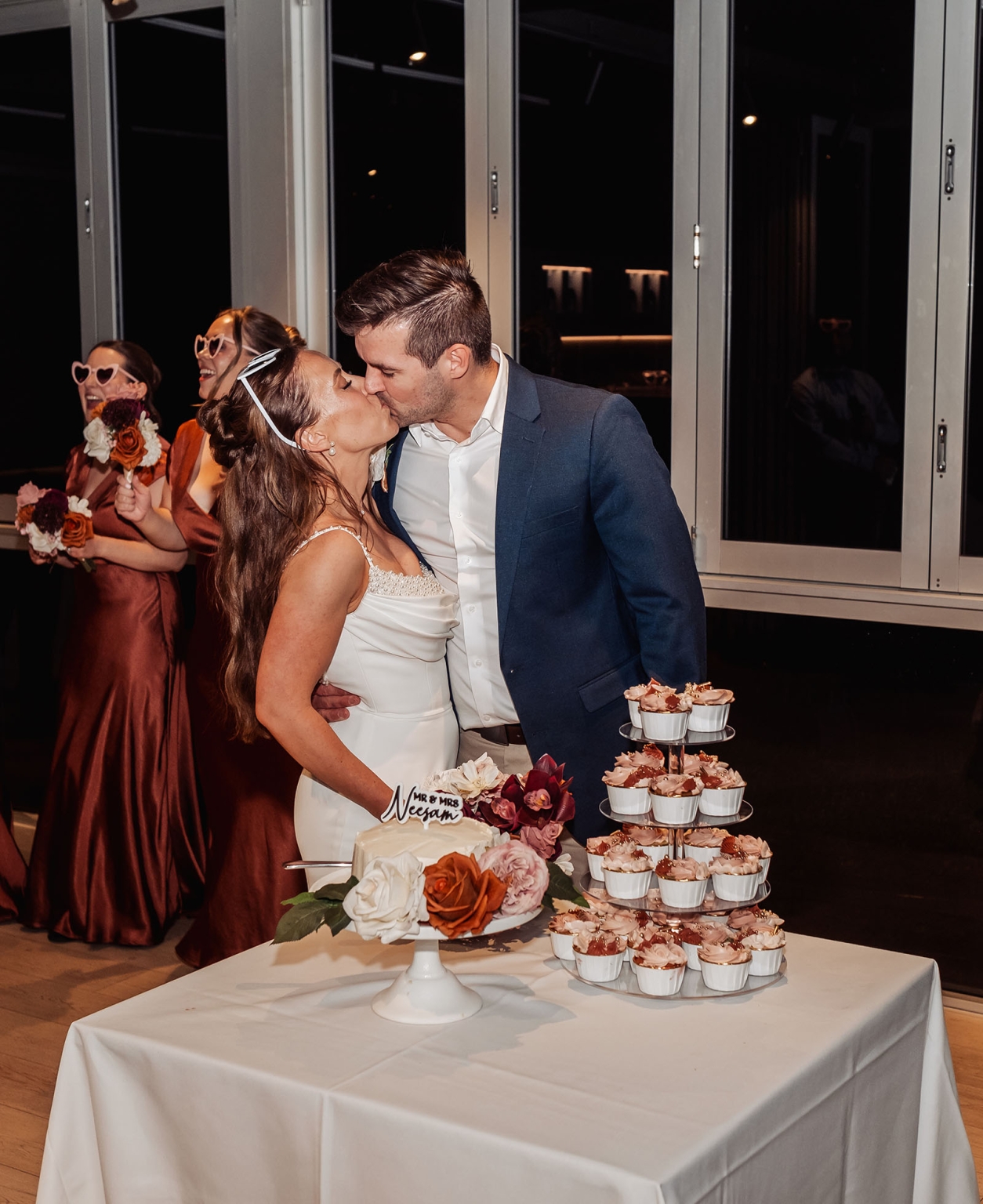 the lane vineyard wedding - caitlyn & craig 132 Bride and groom kiss at wedding with floral cake and joyful bridesmaids.