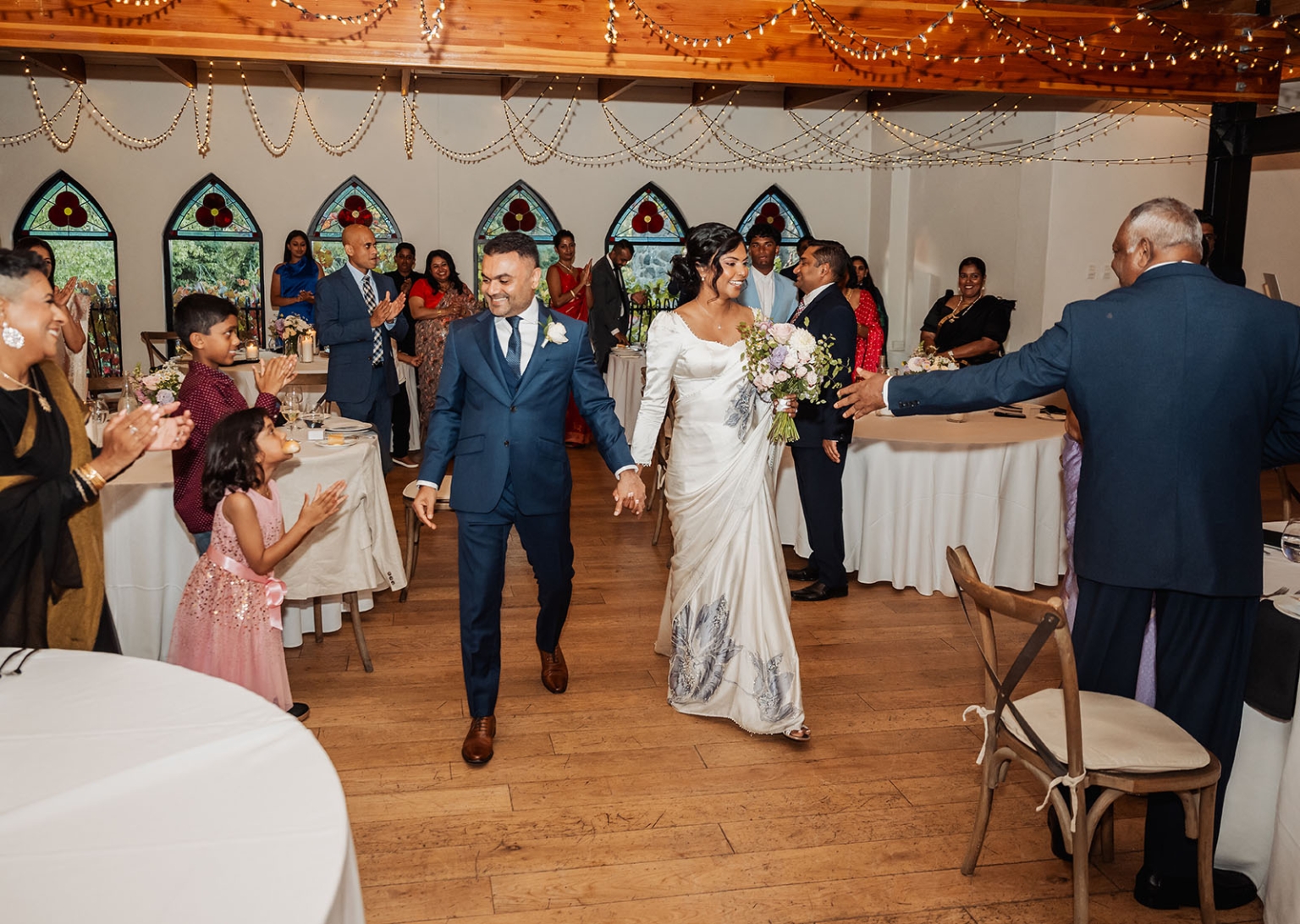 manor wedding in basket range - methmini & aravinda 164 Joyful bride and groom entrance at wedding reception with guests cheering and elegant decor.