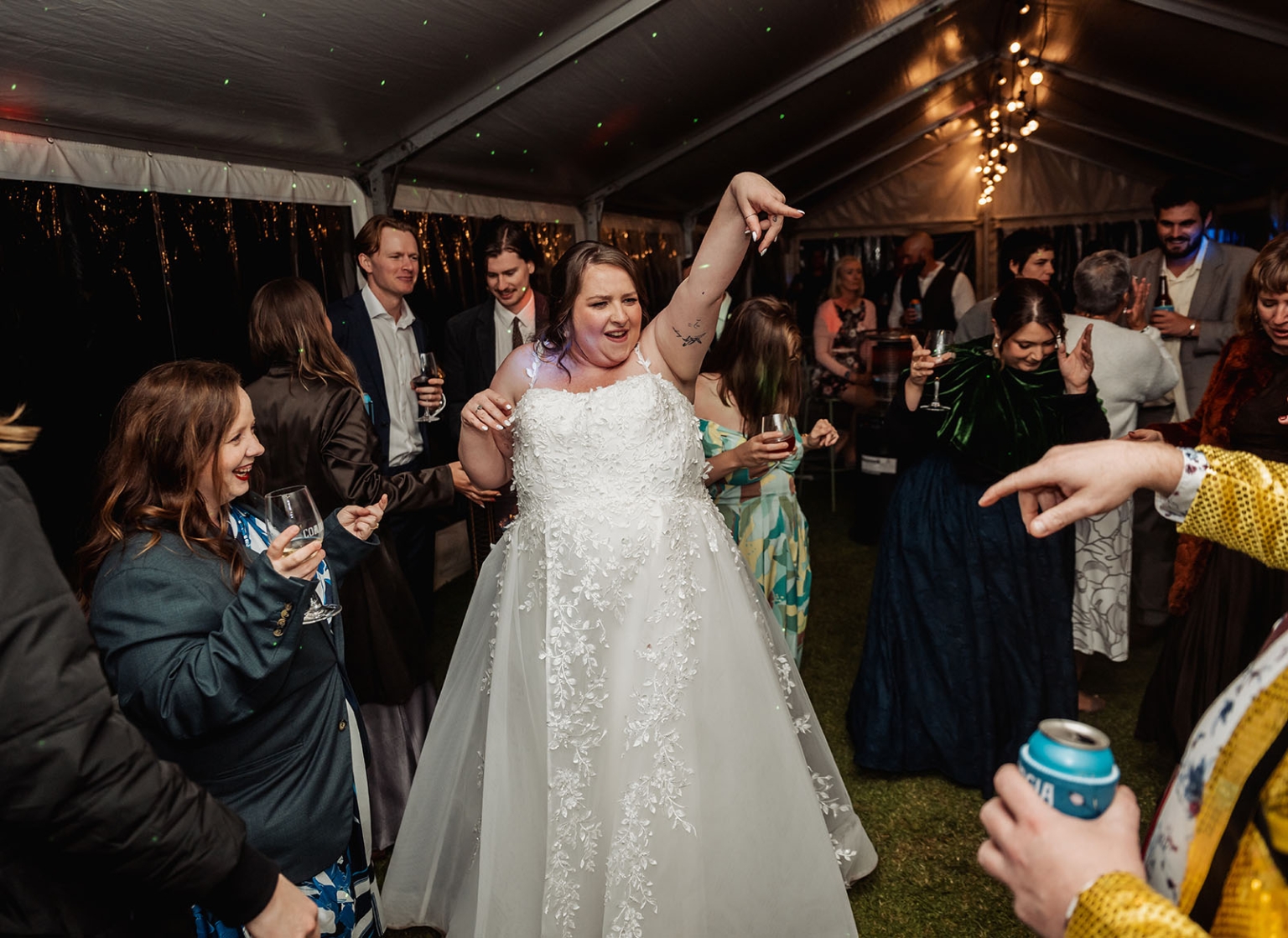 comida wedding - georgia & james 53 Bride dancing joyfully at wedding reception with guests celebrating under warmly lit tent.