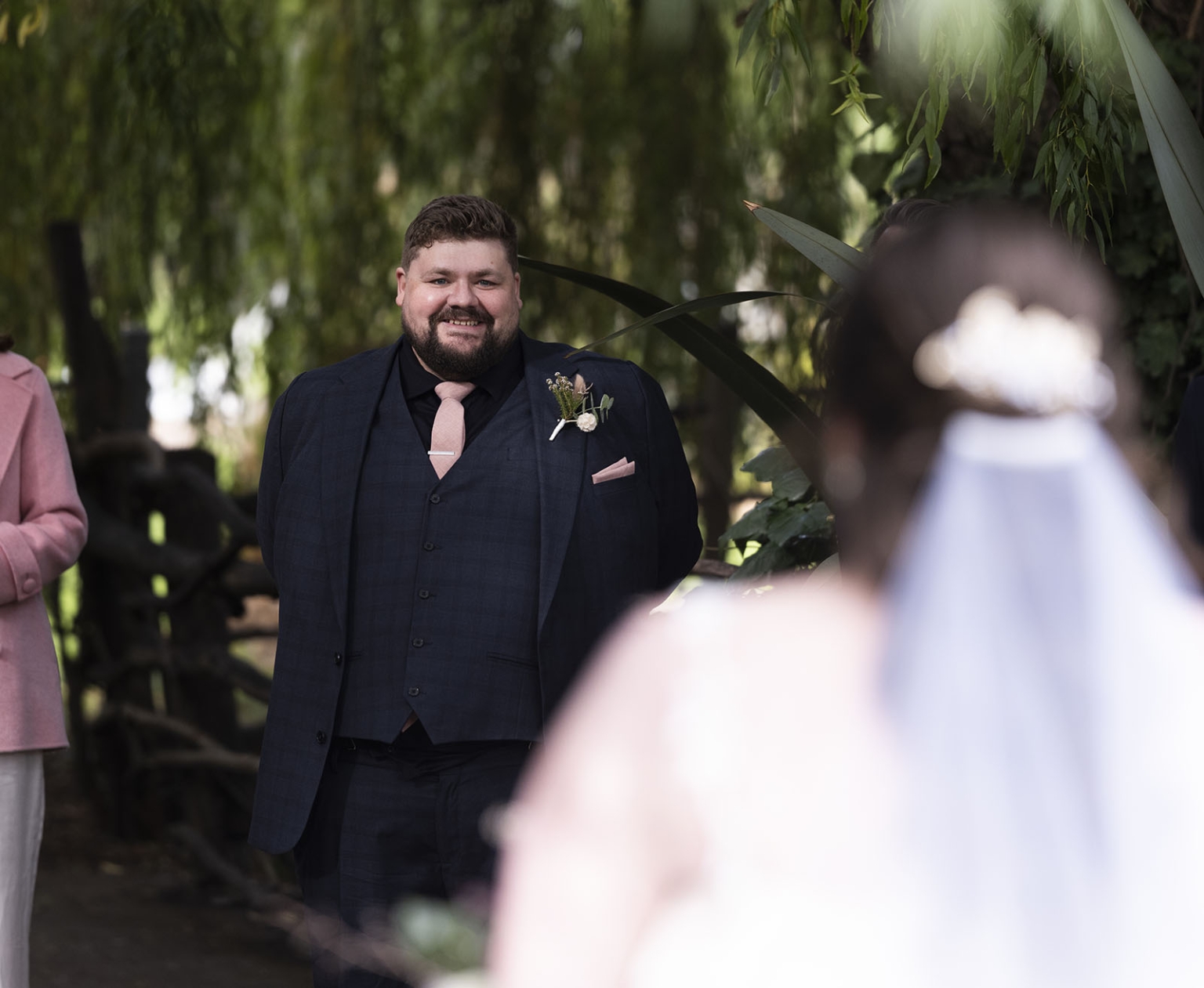 comida wedding - georgia & james 13 Groom smiling at bride under natural archway during outdoor wedding ceremony.