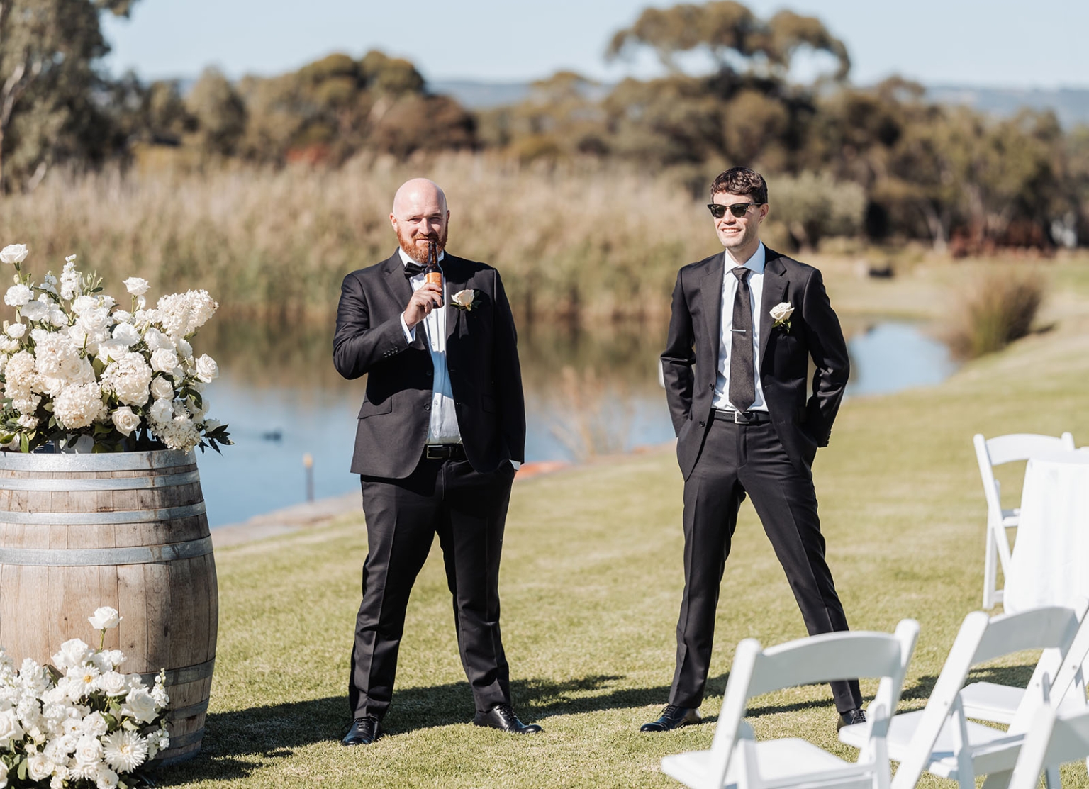 lloyd brothers wedding - dajana & tom 1 Outdoor wedding scene with two men in suits, giving a toast by the water.