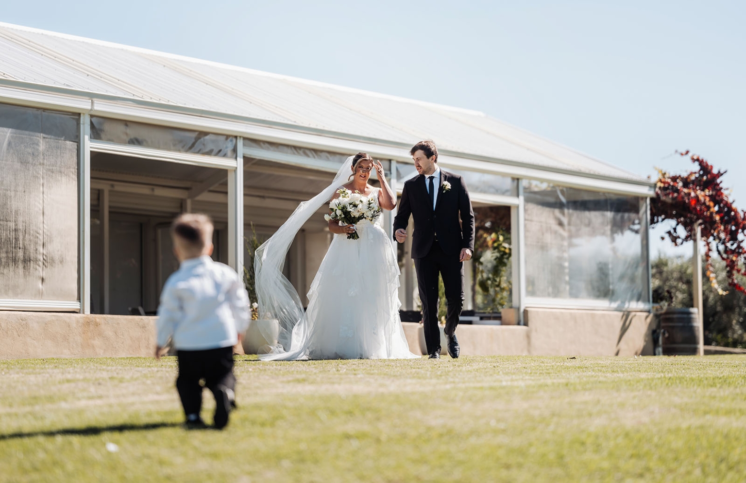 lloyd brothers wedding - dajana & tom 8 Bride and groom walking outdoors, sunny wedding day, elegant white gown, black suit, joyful moment.