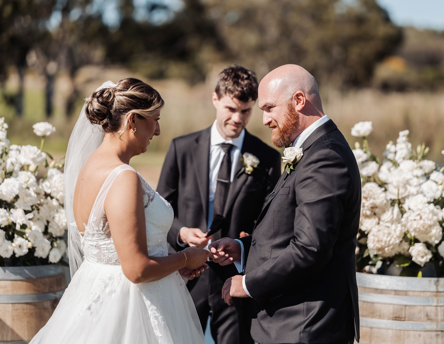 lloyd brothers wedding - dajana & tom 15 Bride and groom exchanging rings at outdoor wedding ceremony with rustic floral decor.