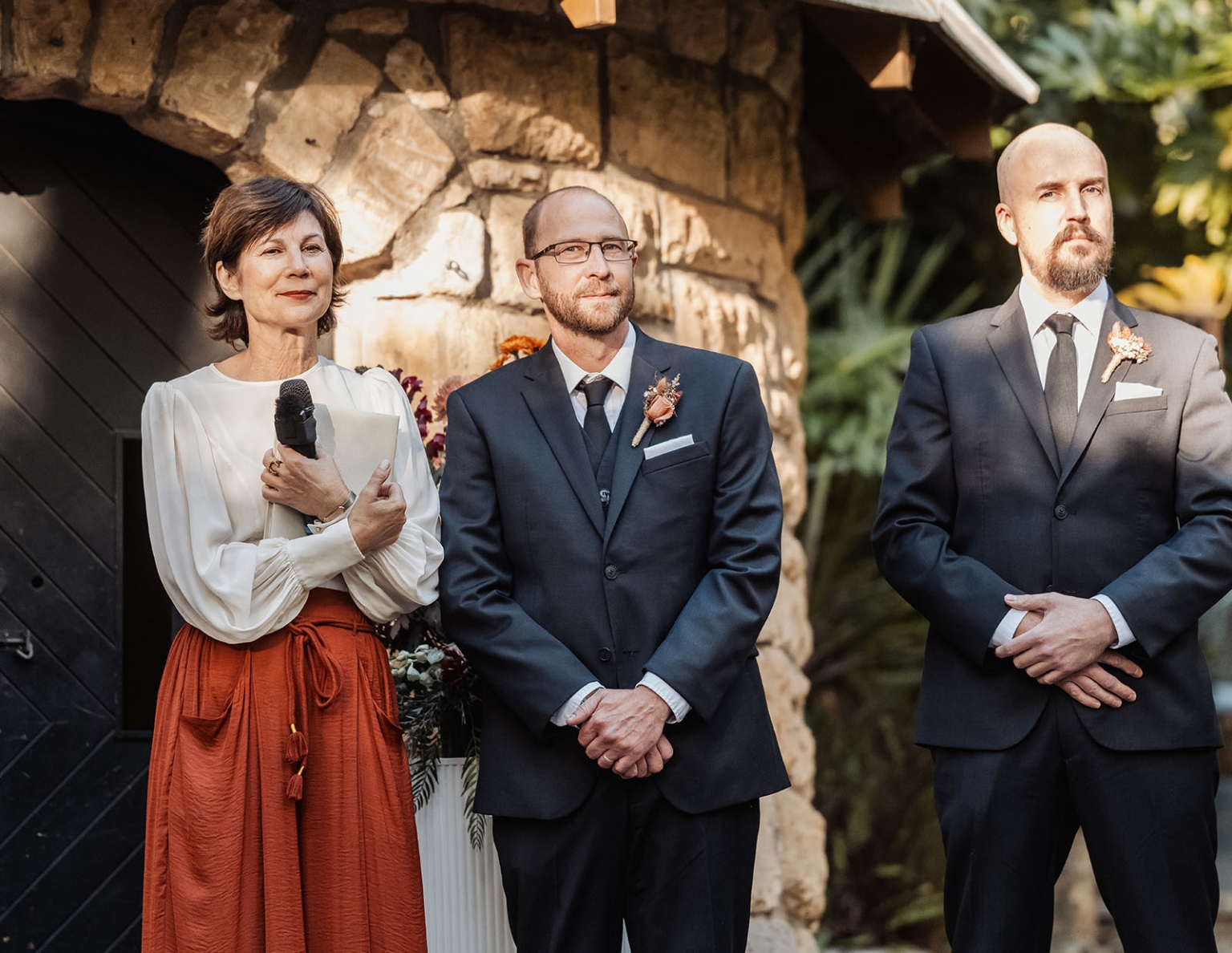 adelaide hills wedding at the manor - jo & dan 20 Outdoor wedding ceremony at rustic stone venue with officiant, groom, and groomsman.