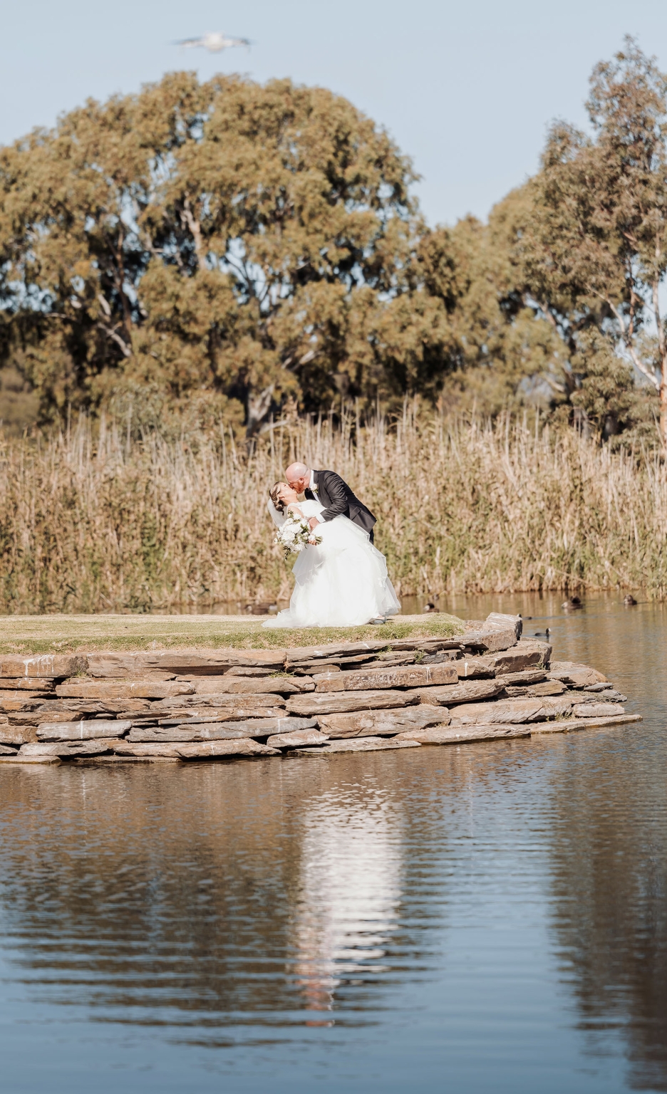 lloyd brothers wedding - dajana & tom 39 Bride and groom kiss by pond, surrounded by nature, reflecting romance and elegance.
