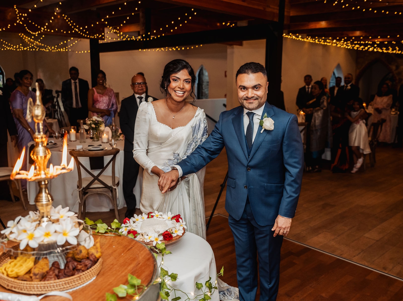 manor wedding in basket range - methmini & aravinda 165 Bride and groom cutting wedding cake surrounded by joyful guests and elegant decor.