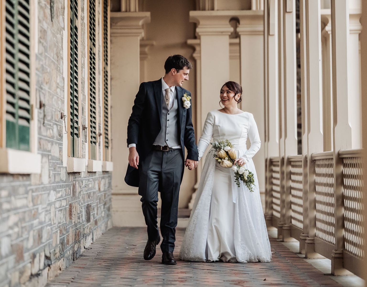 adelaide's st peter's cathedral wedding - irish & nick 44 Bride and groom walking through elegant covered wedding corridor.