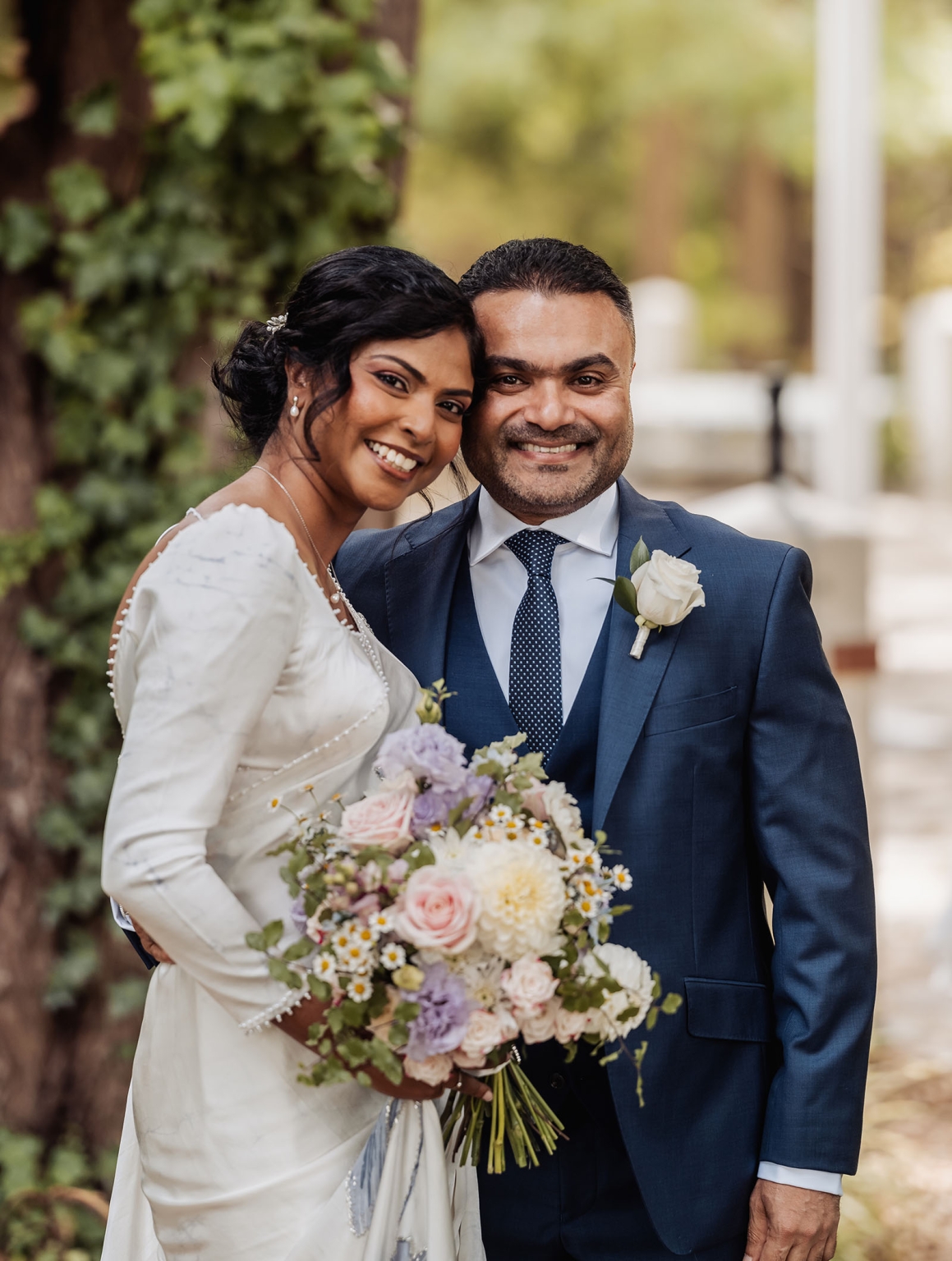 manor wedding in basket range - methmini & aravinda 125 Joyful wedding couple outdoors with white dress and blue suit, holding colorful bouquet.