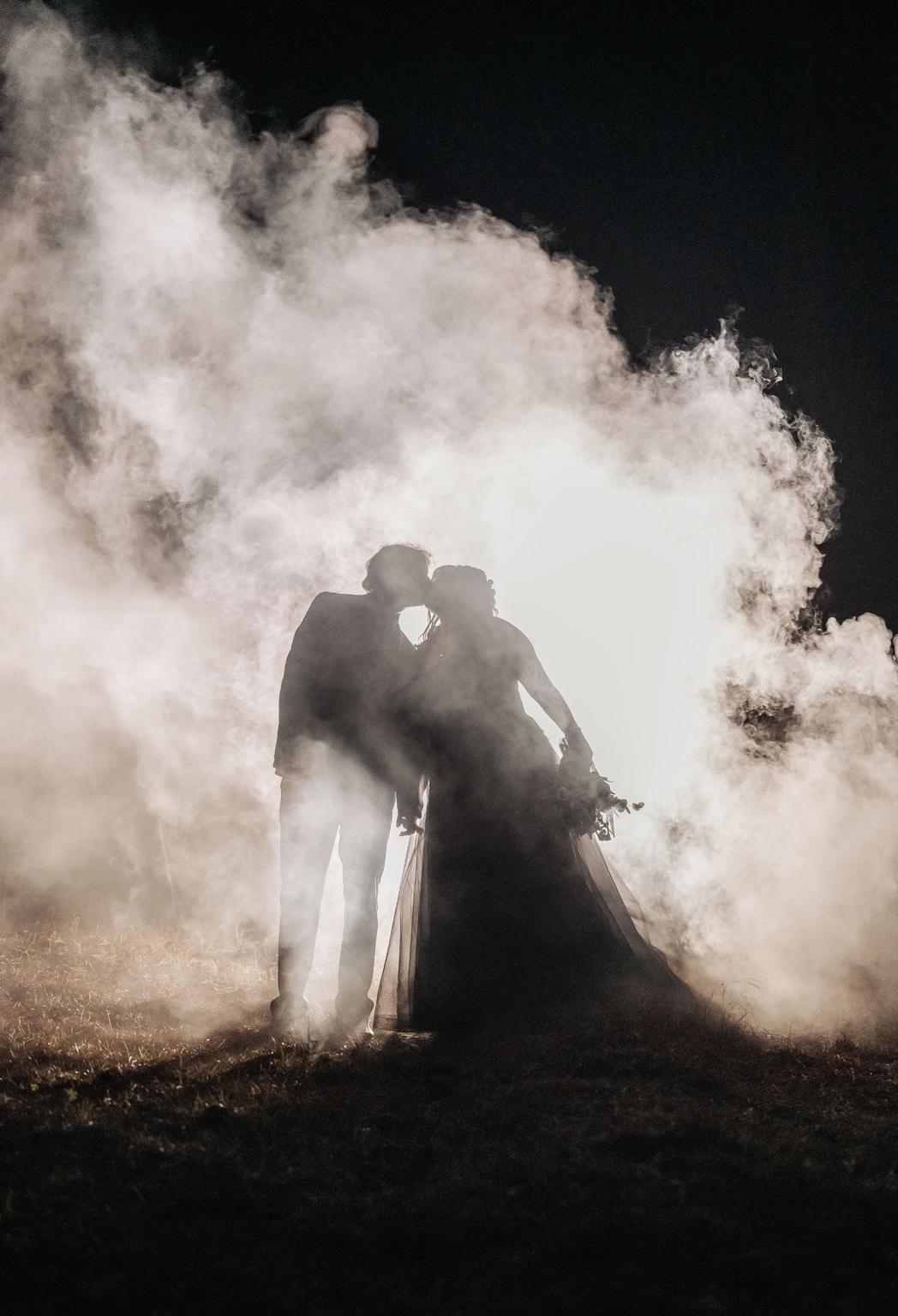 kuitpo forest metal themed wedding – erin & michael 35 Silhouetted wedding couple kissing in smoky nighttime backlit portrait.