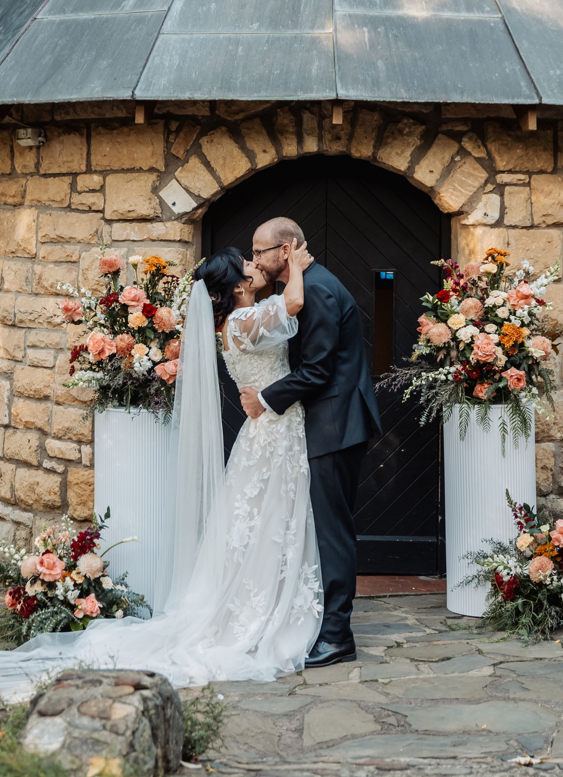 adelaide hills wedding at the manor - jo & dan 29 Bride and groom kissing under rustic stone arch with elegant wedding flowers.