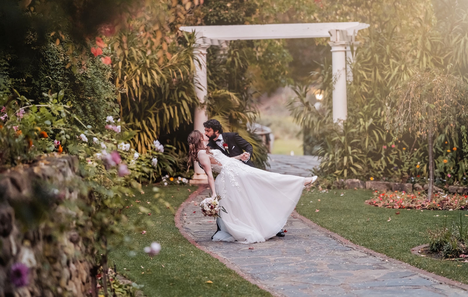 beautiful manor basket range wedding - sophie & theodore 135 Bride and groom embrace in romantic garden wedding scene with archway and flowers.