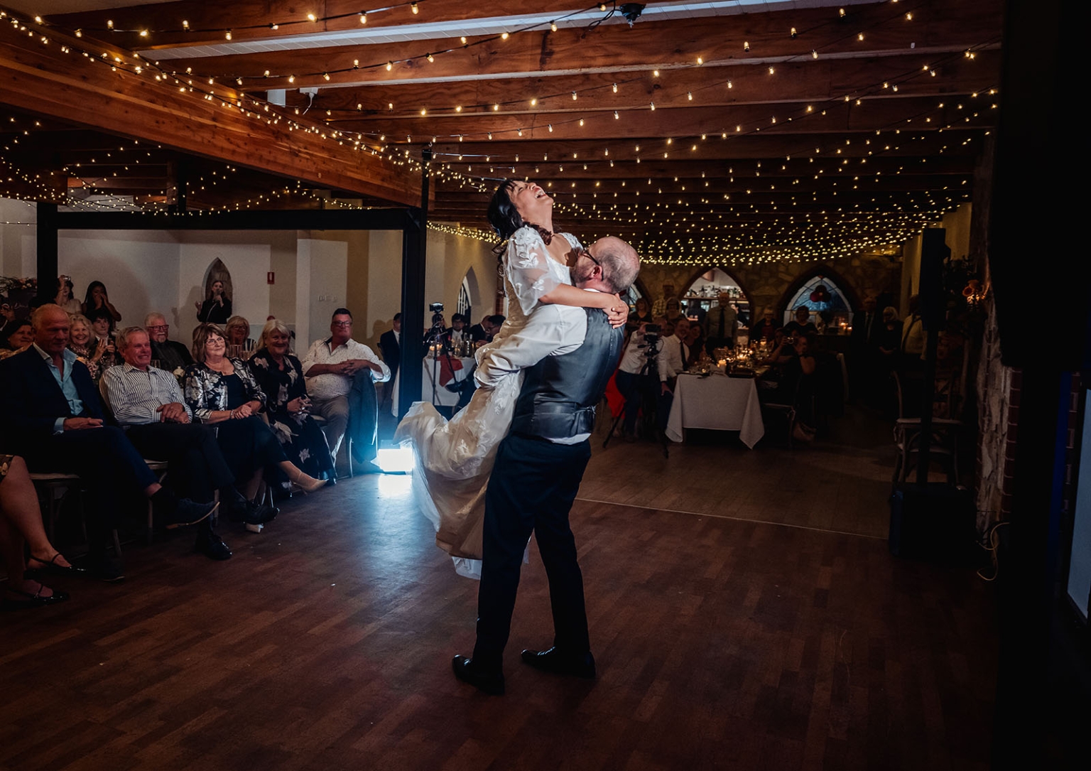 adelaide hills wedding at the manor - jo & dan 71 Bride lifted during joyful wedding dance reception under rustic fairy lights.