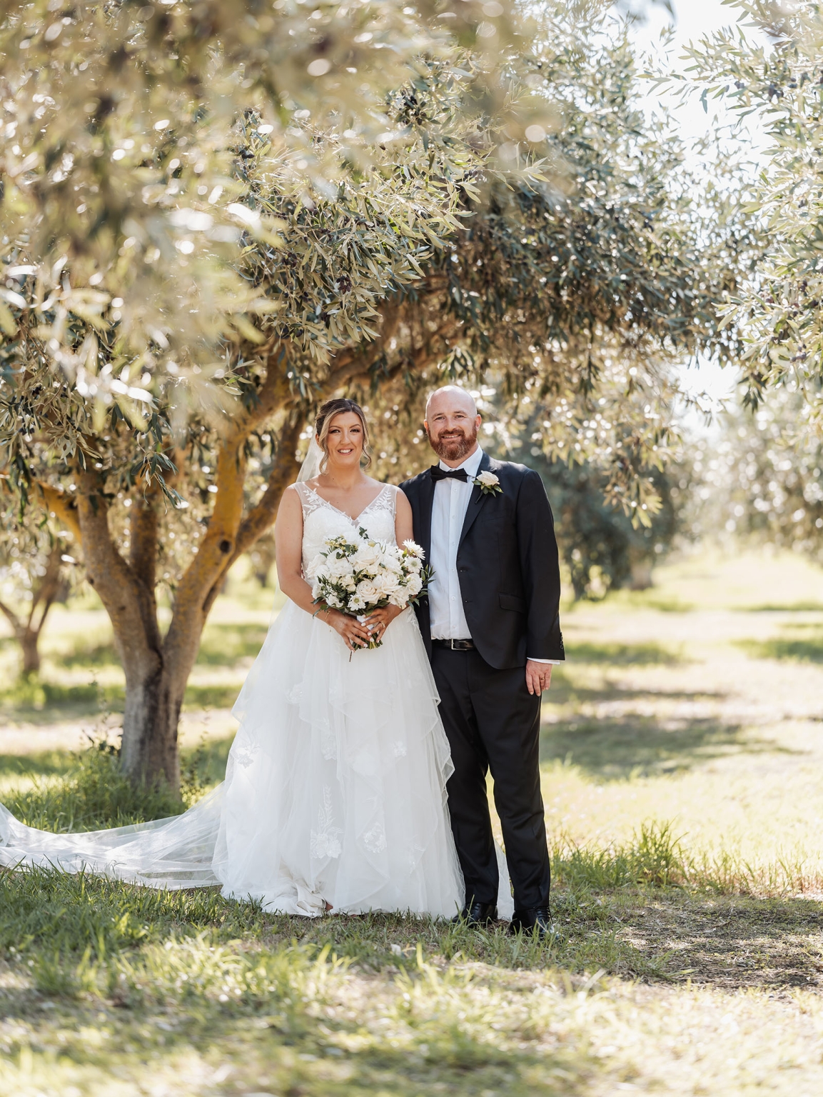 lloyd brothers wedding - dajana & tom 36 Outdoor wedding: couple in elegant attire, sunlit grove, lush trees, romantic moment.
