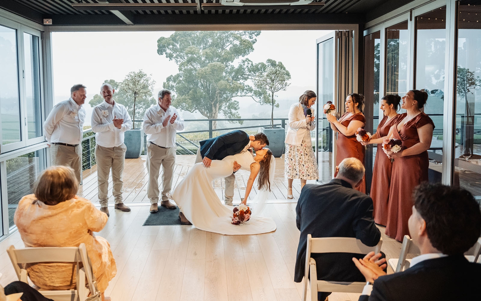 the lane vineyard wedding - caitlyn & craig 124 Bride and groom dip during joyful indoor wedding celebration amidst greenery and guests.