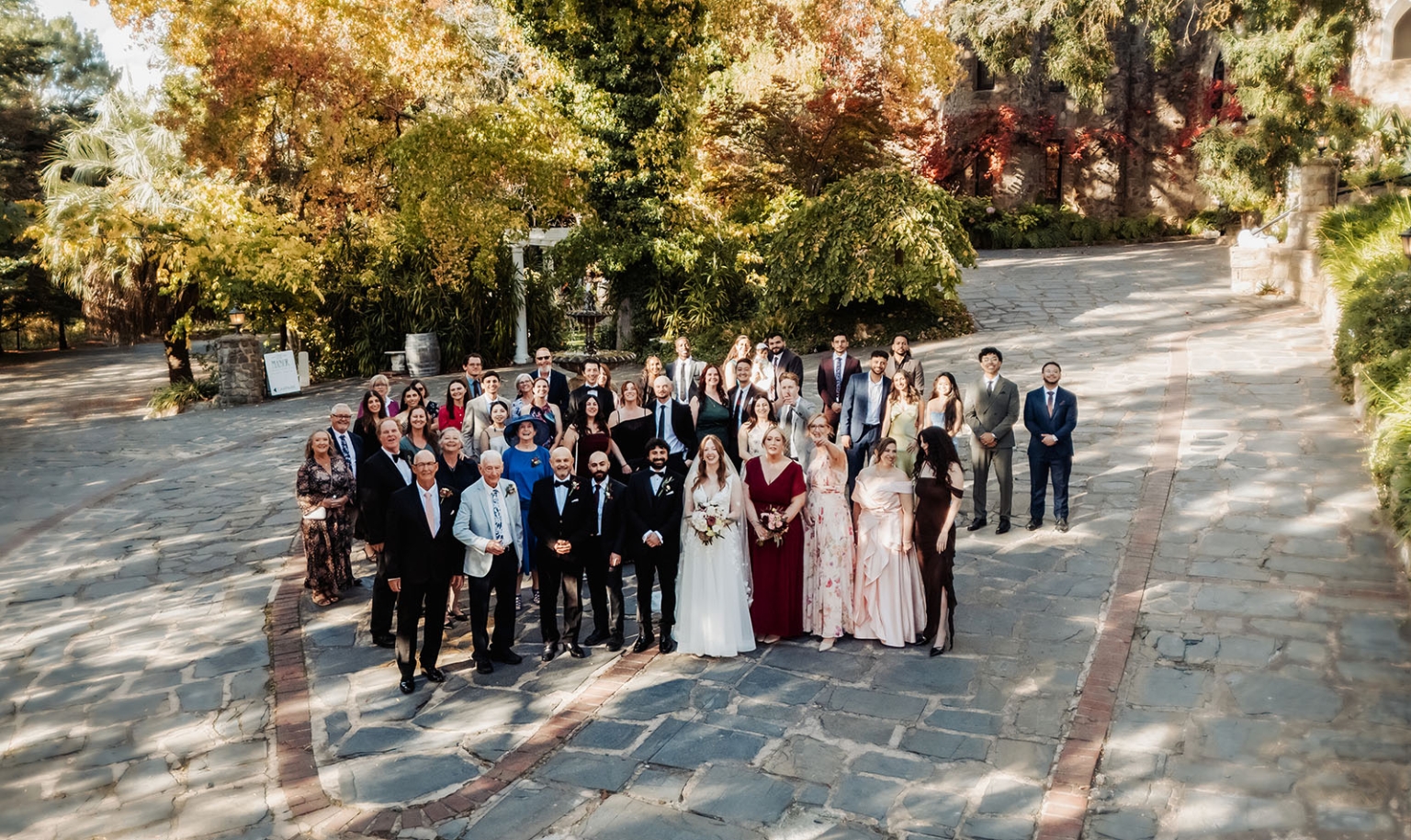 beautiful manor basket range wedding - sophie & theodore 109 Wedding party posing outdoors with autumn foliage and historic stone building.